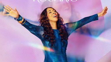 Woman with arms raised in celebration wearing a blue dress against a pink-purple, colorful backdrop.